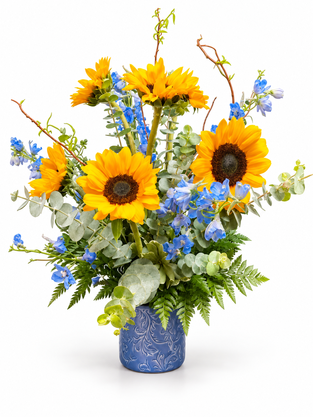 Yellow sunflowers and blue delphinium with eucalyptus in a patterned blue vase on a white background